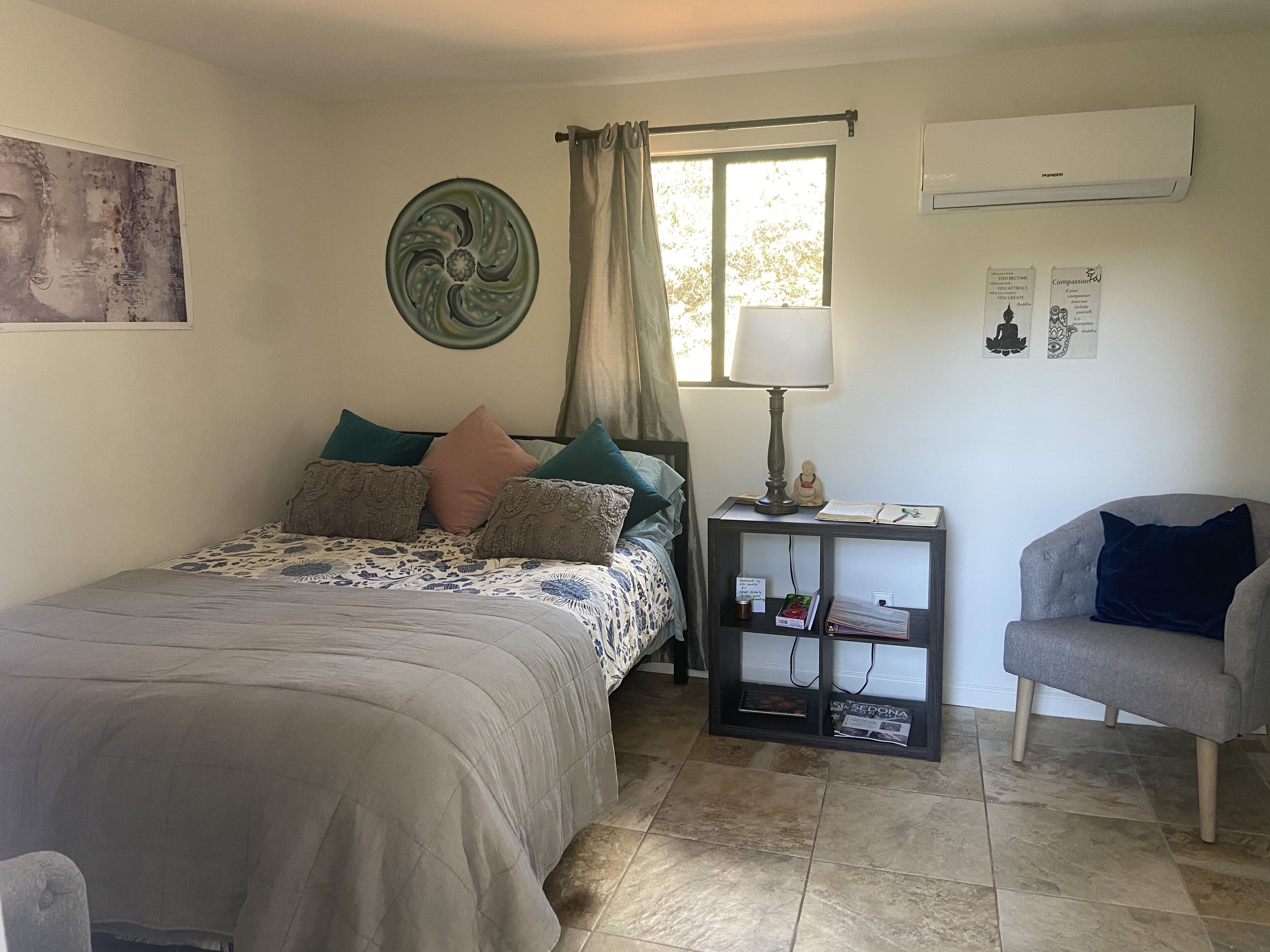 Quarto com cama, mesa de cabeceira com abajur, uma cadeira e janela com cortinas.