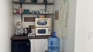 Et lille tekøkken med mikrobølgeovn, brødrister og kaffemaskine. En stor vandkande står på en skammel, og der er et kort på væggen.