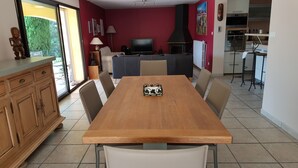 Ein Essbereich mit Holztisch, Stühlen, einem Fernseher und einer Küche im Hintergrund.