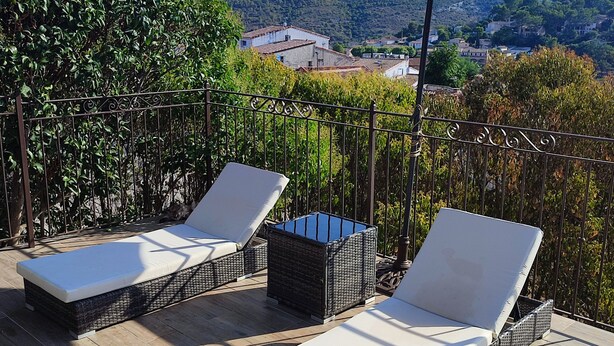 Eine Terrasse mit zwei Liegestühlen und einem großen Sonnenschirm mit Blick auf eine gebirgige Landschaft.