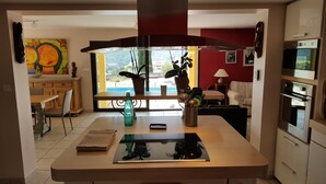 Eine moderne Küche mit einer zentralen Kochinsel, einem Essbereich mit Tisch und Stühlen sowie Blick ins Freie.