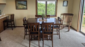 A dining area with a large wooden table, six chairs, a vase with flowers, and a window with a view of greenery. - Fantastic view! Condo located on the Crest of Sugar Mountain (Banner Elk)