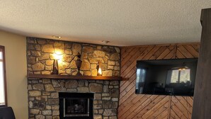 A cozy living room with a stone fireplace, a flat-screen TV mounted on the wall, and a comfortable sofa. - Fantastic view! Condo located on the Crest of Sugar Mountain (Banner Elk)