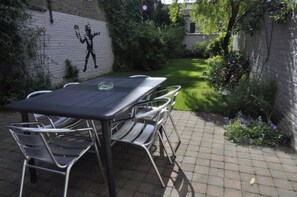Une terrasse extérieure avec une table et des chaises, entourée d’un mur de briques et de verdure.