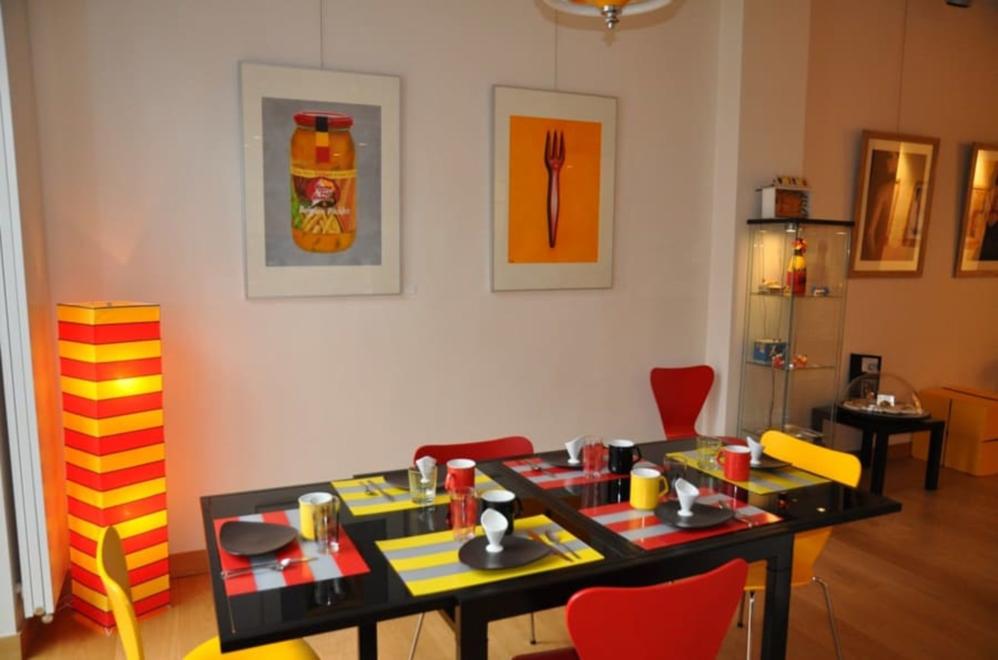 Un coin repas avec une table dressée pour quatre personnes, des chaises et une grande lampe.