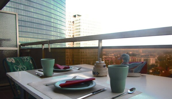 A dining table with plates, cutlery, and a cup, set against a cityscape view.