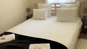 A neatly made bed with white bedding and a black throw blanket, a wooden headboard, and a window with sheer curtains.