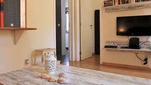 A modern living room with a wooden table, a white decorative vase, and a bookshelf with books.