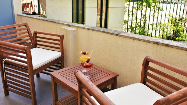A wooden outdoor seating area with two chairs and a table, a drink with fruit, and a view of a building with barred windows.