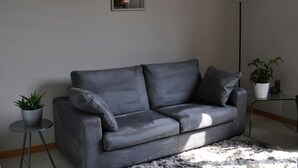 A grey sofa with cushions, a small round table with a plant, a floor lamp, and a framed picture on the wall. - Stylish & Comfortable Apartment in Vibrant Neighborhood –Perfect for Short Stays (Firenze)