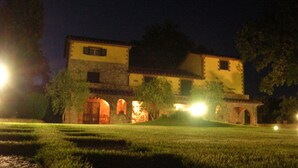 Un edificio de dos pisos con fachada de piedra y arcos, iluminado por luces exteriores.