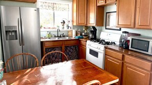 A kitchen with wooden cabinets, a stainless steel refrigerator, a stove, a microwave, and a dining table with chairs.