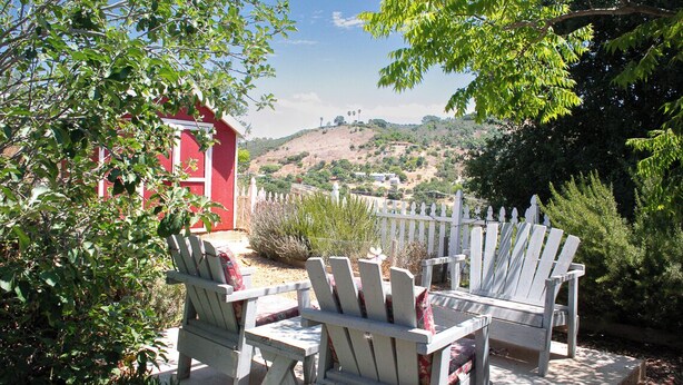 A patio with Adirondack chairs and a red building in the background.