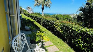 Eine Terrasse mit weißen Stühlen und einem Tisch, eine Palme und Blick aufs Meer.