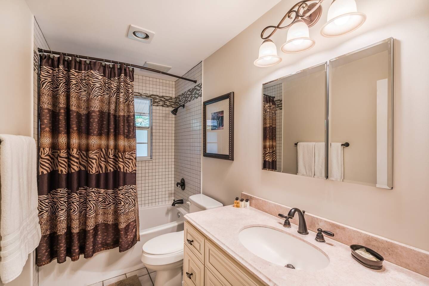 Une salle de bain avec un rideau de douche à motifs zébrés, des toilettes blanches, un lavabo avec un miroir au-dessus et une serviette accrochée au mur.
