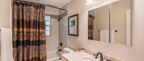 Une salle de bain avec un rideau de douche à motifs zébrés, des toilettes blanches, un lavabo avec un miroir au-dessus et une serviette accrochée au mur.