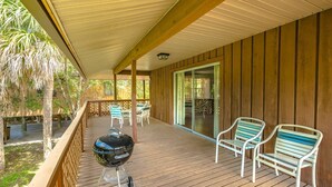 Un espacio al aire libre techado con una terraza de madera, una parrilla y dos sillas.