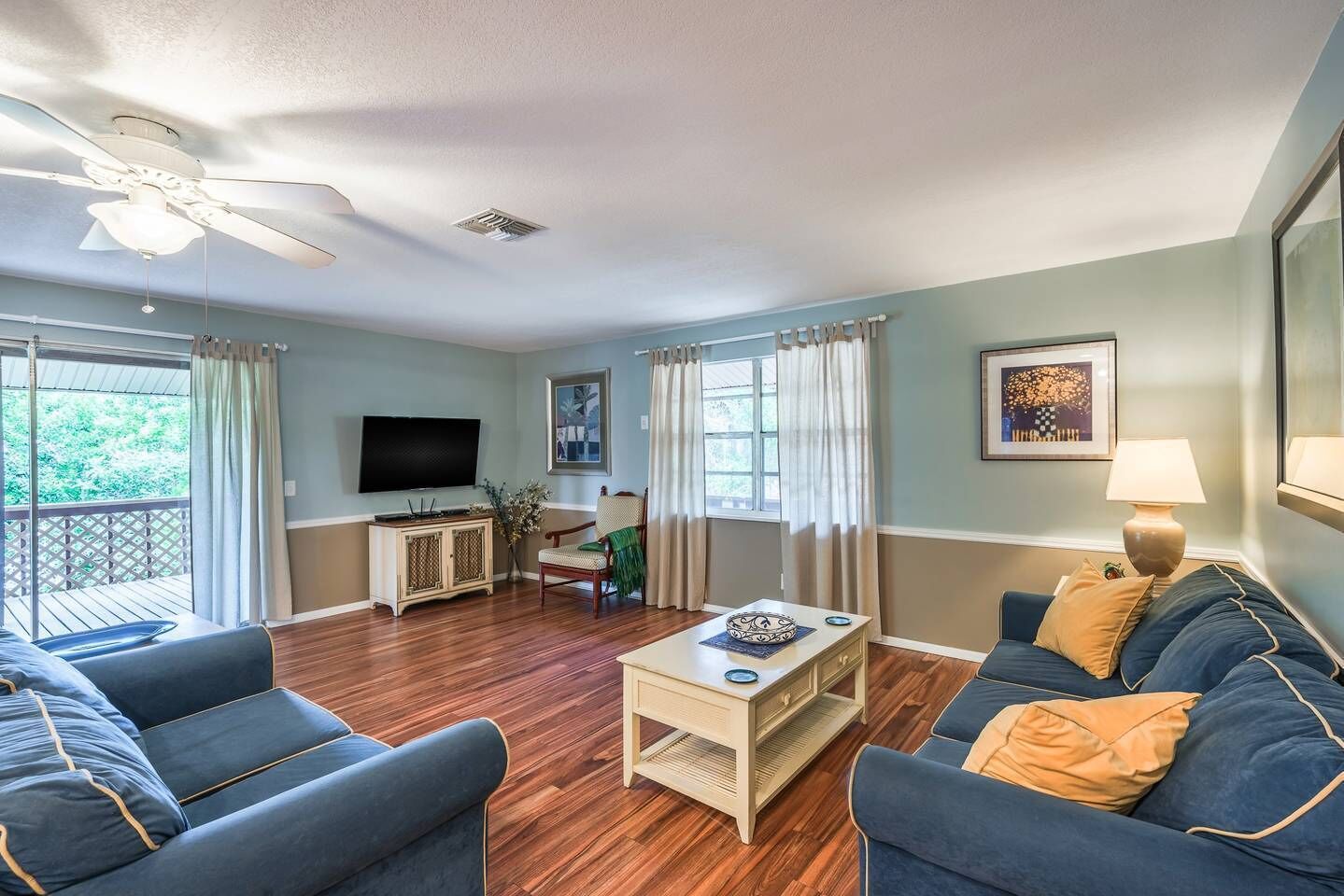A living room with a television, two sofas, a coffee table, and a ceiling fan.