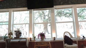 Een kamer met een groot raam, een flatscreen televisie aan het plafond, een rieten stoel en een klein tafeltje met een bloemenvaas.