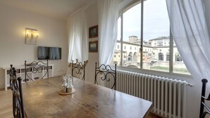 A dining area with a wooden table, metal chairs, a white radiator, and a window with white curtains. - Bardi Apartment, Stunning View Of Ponte Vecchio! (Florence)