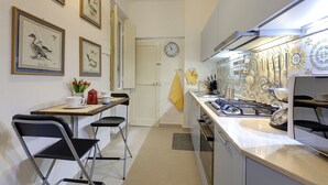 A compact kitchen with a dining area, featuring a clock, framed artwork, and a stove. - Bardi Apartment, Stunning View Of Ponte Vecchio! (Florence)