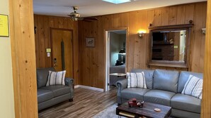 Een gezellige woonkamer met houten lambrisering, een plafondventilator, een open haard en een grote spiegel.