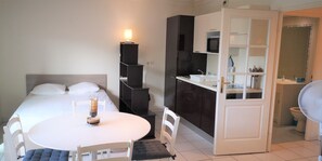 Ein kleines Hotelzimmer mit Bett, Esstisch mit Stühlen, einer kleinen Küchenzeile und einem durchgegangenen Tür erkennbaren Badezimmer.