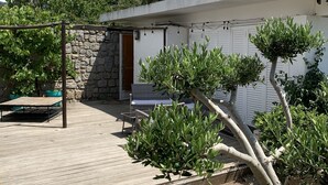 Een binnenplaats met een stenen muur, een houten terras en plantenbakken.