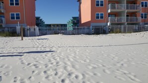 A sandy beach with footprints leading to a gated area with multi-story buildings in the background. - Harbor House-Unit B21-Beachfront Paradise in the Heart of Gulf Shores (Gulf Shores)
