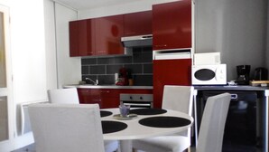 Una cocina pequeña con armarios rojos, una mesa de comedor blanca y sillas.