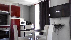 Una cocina moderna con armarios rojos y blancos, un microondas y una cafetera. Hay una zona de comedor con una mesa y sillas blancas, y un televisor de pantalla plana montado en la pared.