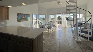 A spacious kitchen with a large island, a dining area with chairs, a spiral staircase, and a balcony with a view. - Walk to the beach! 2 bedroom 2 bath condo with a loft.  (Santa Rosa Beach)