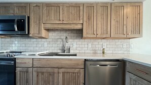 A modern kitchen with wooden cabinets, a stainless steel dishwasher, and a black microwave. - Walk to the beach! 2 bedroom 2 bath condo with a loft.  (Santa Rosa Beach)