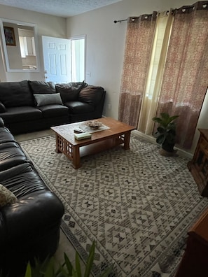 A living room with a dark leather sofa, a wooden coffee table, patterned carpet, and a potted plant. -   Ranch House 3 Blocks to  Beach (Panama City Beach)