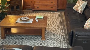 A living room with a television on a wooden cabinet, a coffee table with books and a remote, a sofa with patterned cushions, and a lamp on a side table. -   Ranch House 3 Blocks to  Beach (Panama City Beach)