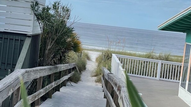 A wooden boardwalk leading to a beach, with a view of the ocean and a building with a green roof. -   Ranch House 3 Blocks to  Beach (Panama City Beach)