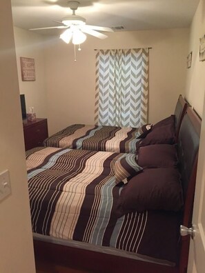 Un dormitorio con cama, ventilador de techo, mesita de noche y cortina con diseño de estampilla.