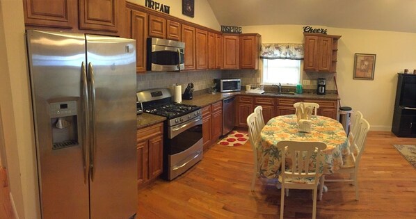 A kitchen with wooden cabinets, stainless steel appliances, a dining table with chairs, and a window with curtains.