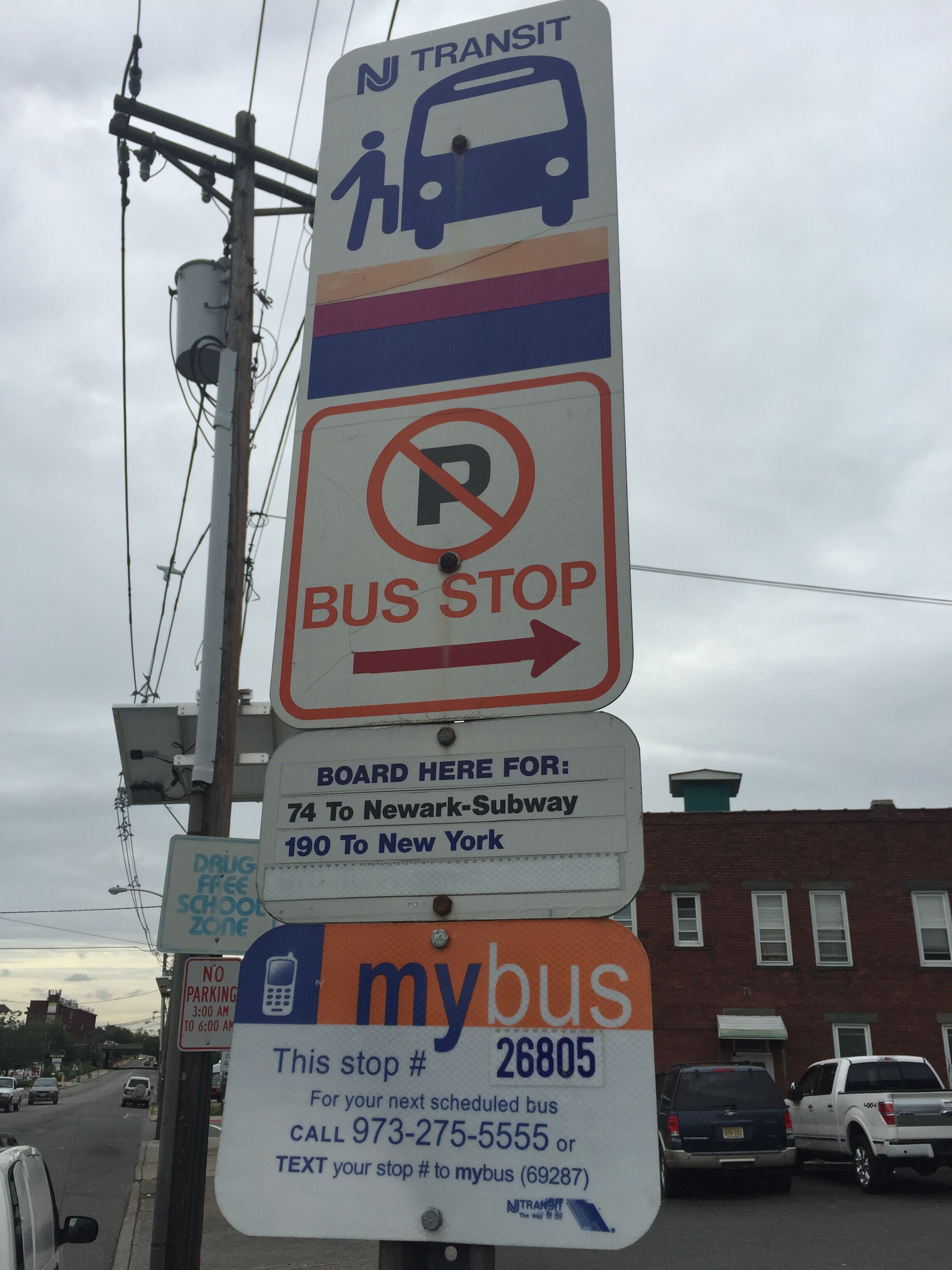 Un panneau d’arrêt de bus indiquant les directions pour rejoindre le métro de Newark et New York, un panneau interdisant le stationnement et un panneau indiquant le numéro d’arrêt MyBus 26805.