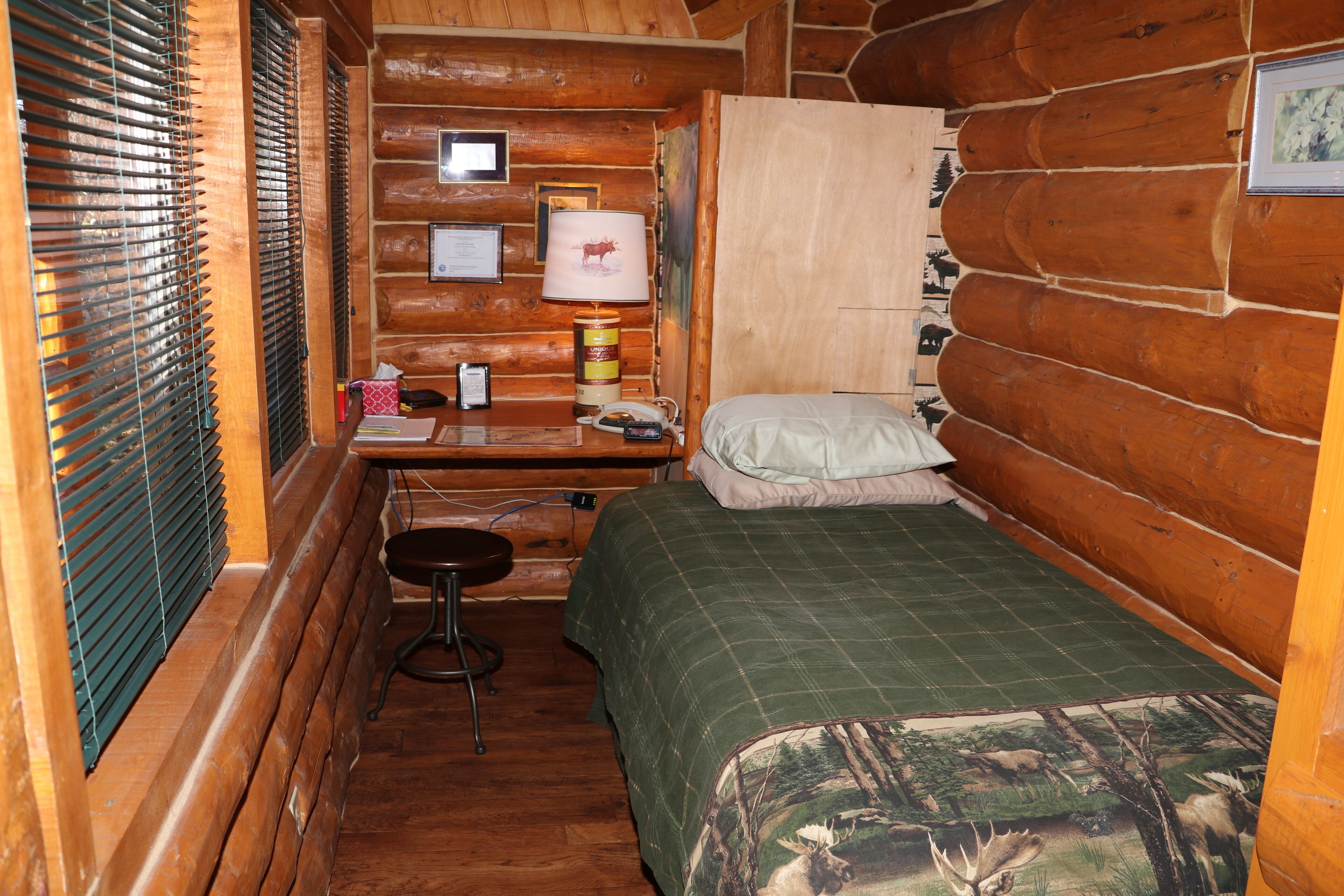 A small cabin room with a bed, a desk with a lamp, and a chair.