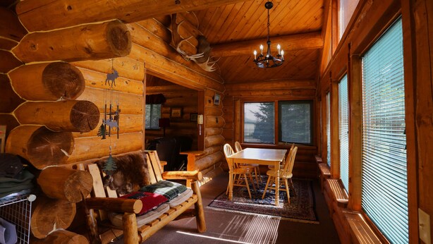 A log cabin interior with a wooden dining table, chairs, a sofa, and a chandelier. - Moose - Unique Alaskan log home in trees & wildflowers on 14-acre homestead. (Anchor Point)