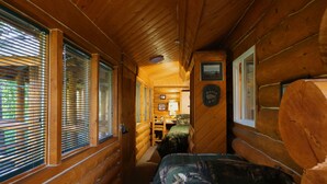 A log cabin interior with a narrow hallway, wooden walls, and a bed with a camouflage cover. - Moose - Unique Alaskan log home in trees & wildflowers on 14-acre homestead. (Anchor Point)