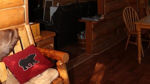 A wooden cabin interior with a dining area, a fireplace, and a ceiling mounted deer antler. - Moose - Unique Alaskan log home in trees & wildflowers on 14-acre homestead. (Anchor Point)