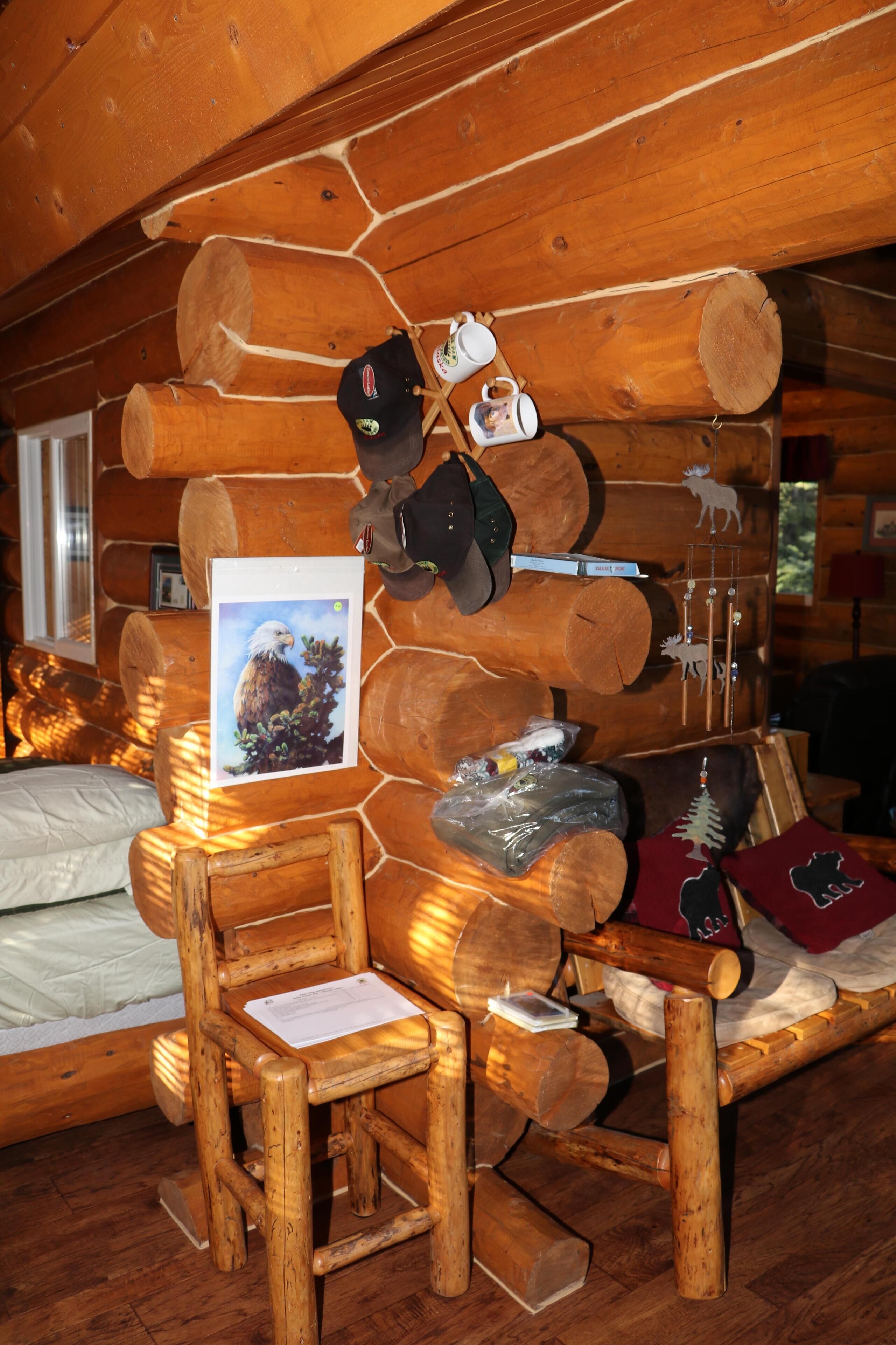 Une chambre de style rustique, avec un lit en bois, une chaise en bois, une table en bois et un mur décoré de rondins de bois, d’une image encadrée et de divers objets.