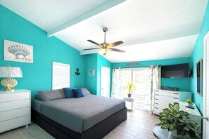 A bedroom with a bed, a ceiling fan, a TV, a plant, and a window with curtains.