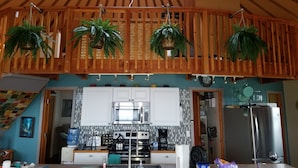 A kitchen with wooden ceiling beams, hanging plants, a stove, microwave, and a refrigerator. -  New Round House With Pool 180 Degree Ocean View 13% discount for 7 nights  (Captain Cook)