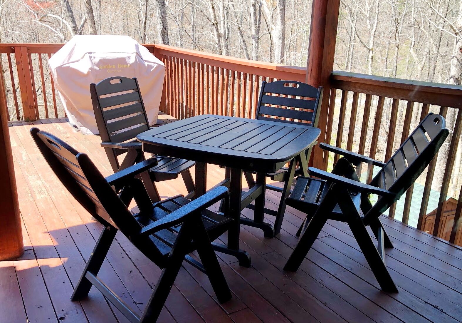 A wooden deck with a table and four chairs, a barbecue grill, and a wooden railing.