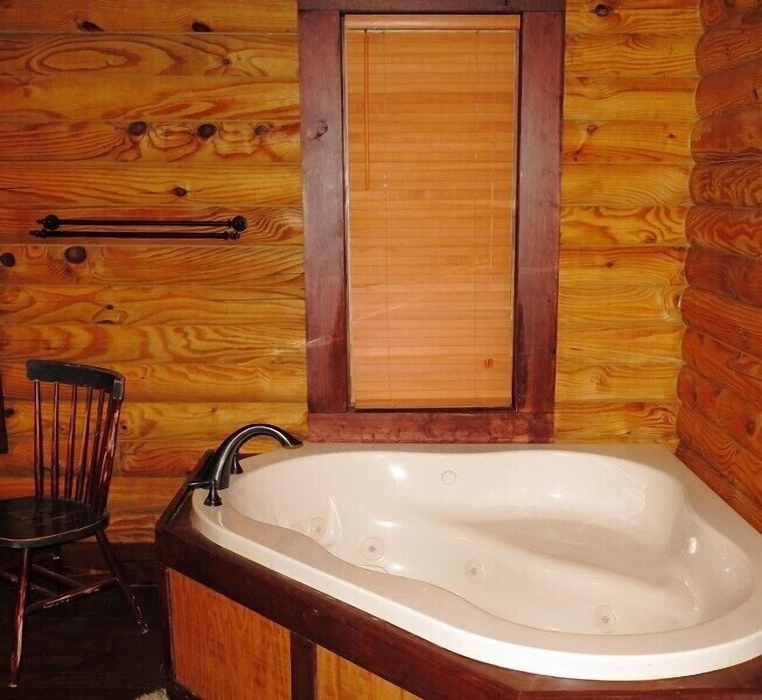 A wooden cabin interior with a bathtub, wooden walls, a wooden door, and a wooden chair.