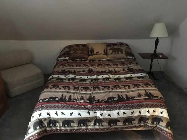Una cama con una colcha estampada, una mesita de noche con una lámpara y una silla.