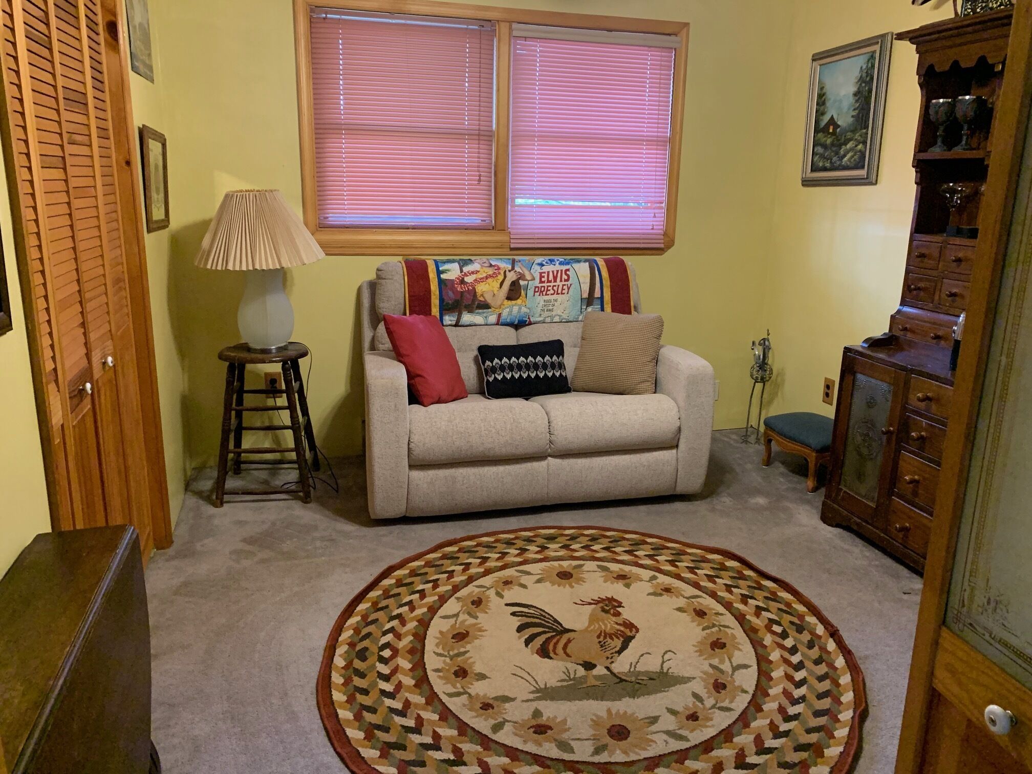 A living room with a beige sofa, a wooden cabinet, a lamp, and a rug with a rooster design.